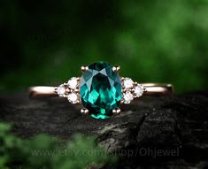 an emerald colored ring with white diamonds on top and green leaves in the back ground