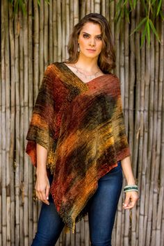 a woman standing in front of a bamboo fence wearing a colorful ponchy shawl