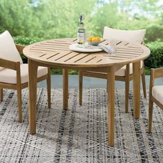 a wooden table with four chairs and a bottle of beer on it in front of some bushes