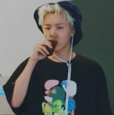 a young man with blonde hair drinking from a wine glass while standing in front of a computer