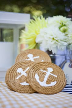 three brown coasters with white anchors on them sitting on a checkered tablecloth