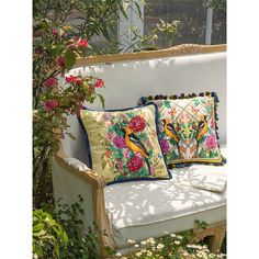 two pillows sitting on top of a white couch in front of flowers and greenery