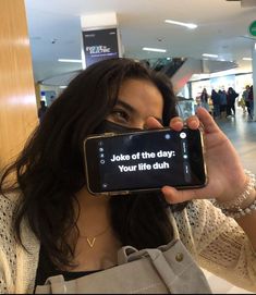 a woman holding up a cell phone with the text joke of the day on it