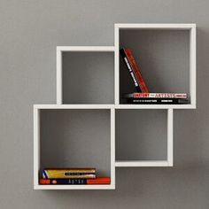 three white cube shelves with books on each shelf and a clock in the middle, against a gray wall