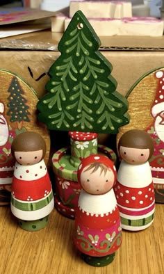 three wooden christmas decorations sitting on top of a table next to a box with a tree in it