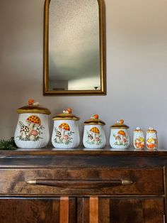 a wooden dresser topped with lots of ceramic jars filled with different types of mushrooms and plants