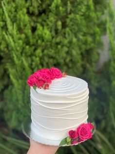 a hand holding a white cake with pink flowers on top and greenery in the background