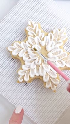 someone is decorating a snowflake cookie with white icing on a sheet of paper