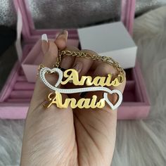 a hand holding a gold and silver name necklace with two hearts in the shape of an arrow