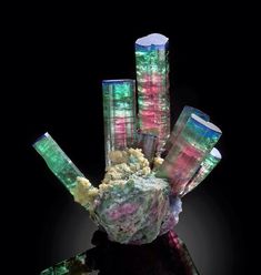 some very pretty colorful rocks in a glass vase on a black background with light coming through it