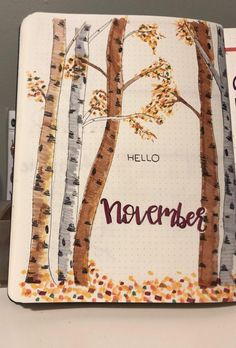 an open notebook with the words hello november written on it and trees painted in autumn colors