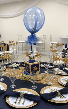 a table set up for a birthday party with blue and gold decorations, silverware, and balloons