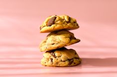 three chocolate chip cookies stacked on top of each other in front of a pink background