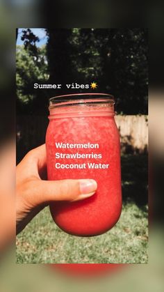 a hand holding a red mason jar filled with watermelon strawberries and coconut water