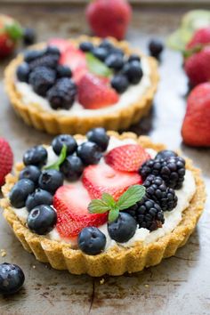 two tarts topped with berries and blueberries on top of a baking sheet next to strawberries