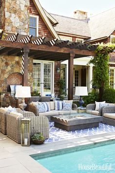 an outdoor living area with couches and tables next to a swimming pool in front of a house