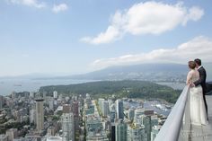 a bride and groom standing on the edge of a balcony overlooking a cityscape