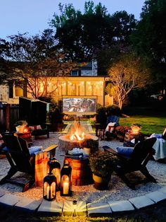 a fire pit surrounded by lawn chairs and candles in front of a house at night