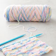 two skeins of yarn next to a crochet hook and knitting needles