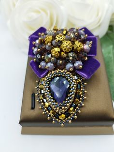 a purple brooch sitting on top of a brown box next to white roses and flowers