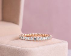 a rose gold wedding band with white diamonds on the inside and outside, sitting on a pink velvet chair