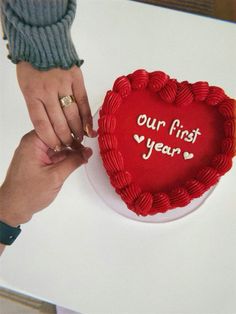 two hands holding a heart shaped cake with the words our first year written on it