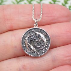 a person is holding a silver coin with two dolphins on it's back and the other hand has a chain