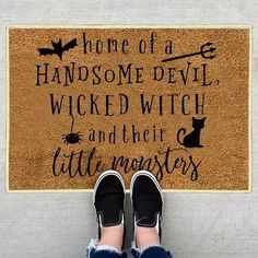 someone standing in front of a door mat that says home of a handsome devil, wickd witch and their little monsters