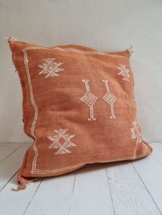 an orange pillow with white embroidered designs on the front and back, sitting on a wooden floor