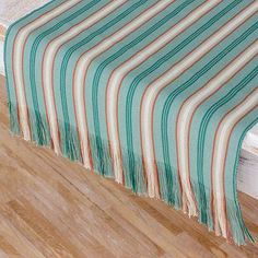 a bed with a green and white striped blanket on it's side next to a wooden floor