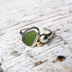 This cluster ring is truly unique. It consists of a bezel set green piece of sea glass, a silver pebble and solid 9ct gold blob. The ring band is a uk size n and a half and the ring is 3mm in width. The sea glass is 12 x 8mm at its widest points and the silver pebble is 4mm in diameter. The ring has a beautiful polished finish and comes presented in a gift box making a perfect gift. It's in stock and will be dispatched within 1-3 working days via Royal Mail Recorded. Silver Handmade Ring, Sea Pottery Jewelry, Silver Smithing Jewelry, Sea Glass Rings, Silversmithing Jewelry, Pebble Ring, Sea Glass Ring, Silver Rings With Stones, Bezel Set Ring