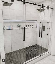 a walk in shower sitting next to a white tiled wall and floor with black accents