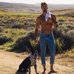 a man with no shirt standing next to a dog on a dirt road in the desert