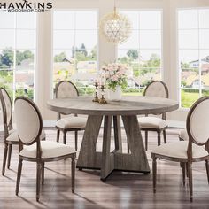 a round table with chairs around it in front of large windows and wooden flooring