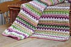 a crocheted blanket sitting on top of a wooden table next to a wicker basket