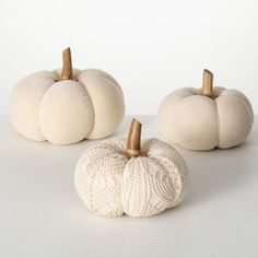 three white knit pumpkins sitting on top of a table