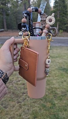 a person holding a coffee cup with jewelry hanging from it's side and a cell phone in the other hand