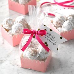 three pink boxes filled with white chocolate covered donuts and a red ribbon tied around the top