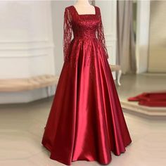 Step into timeless elegance with our exquisite Red Satin Evening Gown. Designed with a sophisticated square neckline and adorned with intricate beadwork, this gown is the epitome of chic. The long sleeves feature sheer, beaded detailing that adds an ethereal touch, making it perfect for formal events, galas, or upscale parties.Crafted from premium quality satin, this dress offers a luxurious gleam and a comfortable fit, allowing you to move with grace and confidence. The full-length, A-line silhouette flatters all body types, while the cinched waist accentuates your natural curves, creating a stunning hourglass figure. The fabrics rich, deep red hue is both bold and timeless, ensuring you stand out in any crowd.Pair this glamorous gown with your favorite accessories and heels for a complet Long Sleeve Satin Gown For Gala, Square Neck Embellished Dresses For Formal Events, Long Sleeve Satin Gala Gown, Embellished Gown With Fitted Bodice And Long Sleeves, Long Sleeve Gown With Embellished Fitted Bodice, Embellished Long Sleeve Gown With Fitted Bodice, Red Long Sleeve Evening Dress With Fitted Bodice, Long Sleeve Satin Gown With Sweep Train, Red Long Sleeve Evening Dress With Sweep Train