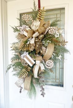 a christmas wreath hanging on the front door with pine cones, evergreens and ribbons