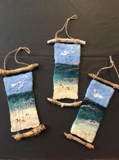 three pieces of fabric hanging from twine with sea and beach scenes on them,