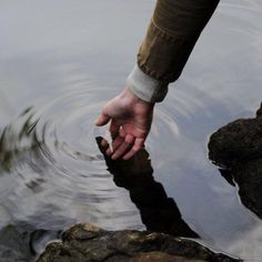 a person reaching for something in the water with their hand on top of some rocks