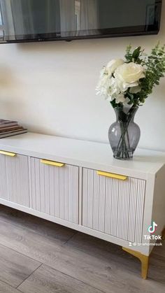 a vase with white flowers sitting on top of a dresser next to a tv mounted above it