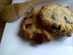 two chocolate chip cookies sitting on top of a white plate next to a wooden spoon