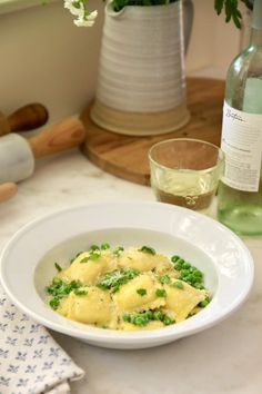 a white bowl filled with pasta and broccoli next to a bottle of wine