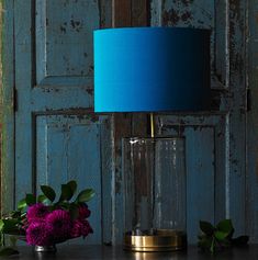 a blue lamp sitting on top of a table next to a vase filled with flowers