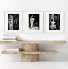 three black and white photographs hang on the wall above a shelf with books, magazines and a clock