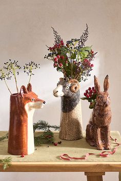 three ceramic animals are sitting on a table with flowers and berries in the vases