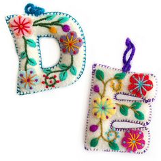 two embroidered letters with flowers on them and one has a string hanging from the bottom