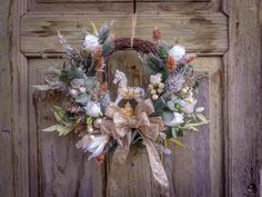 a wreath with white flowers and greenery hanging on a wooden door, decorated with gold ribbon